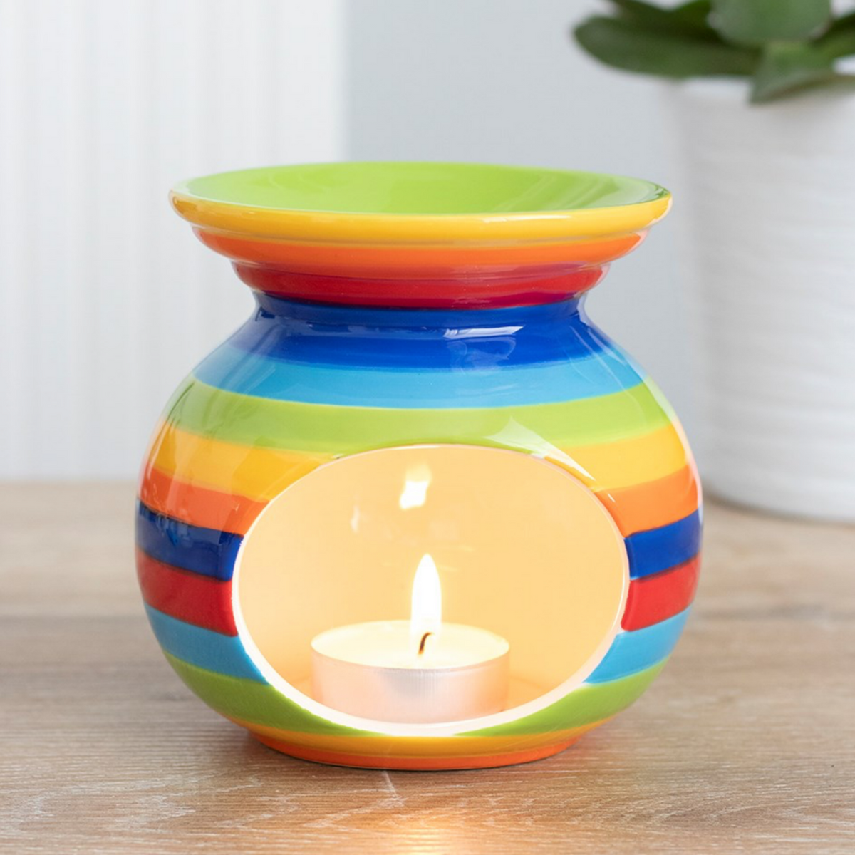 Rainbow striped wax melt warmer with a lit tealight in its open base