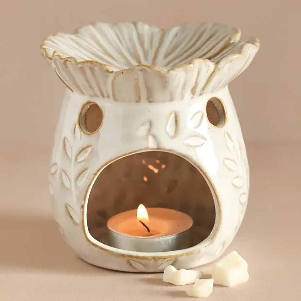 Cream ceramic wax melt warmer with a flower-shaped dish, floral cutouts and a lit tealight