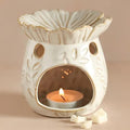 Cream ceramic wax melt warmer with a flower-shaped dish, floral cutouts and a lit tealight